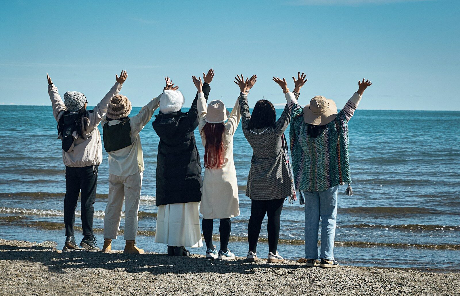 Seven people with arms raised on a beach
